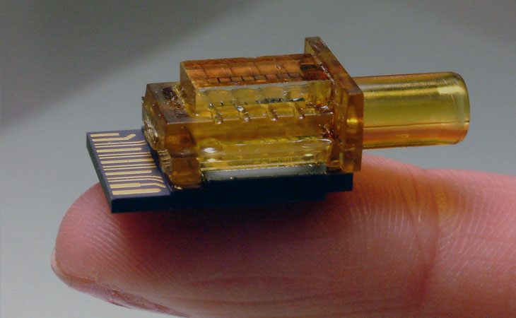 An orange optical subassembly (OSA) resting on someone's finger tip.
