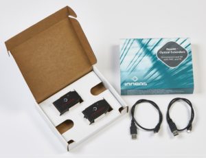 An open cardboard box with a black extender resting inside with another box and black fiber cables next to it.