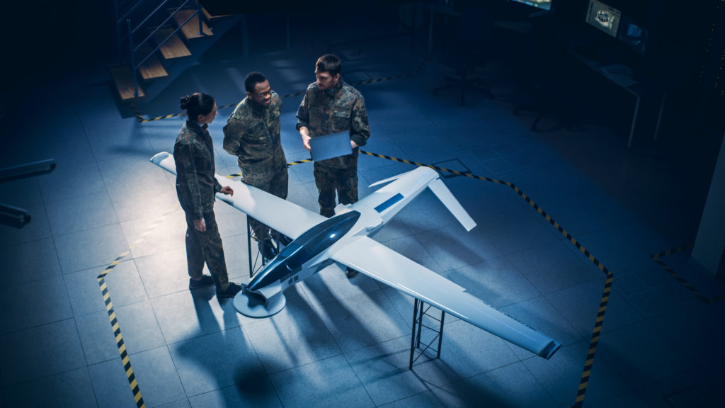Three military professionals standing around a model air plane