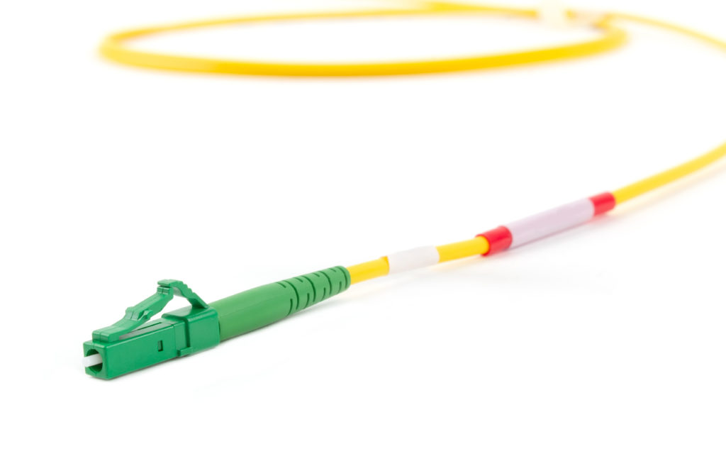 Single mode fiber optic cable with green LC connector isolated on white background.