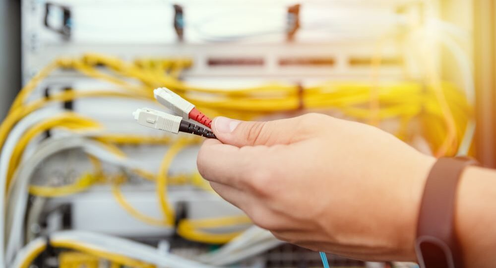 Hand holding two yellow fiber cables with optical connectors on the ends.