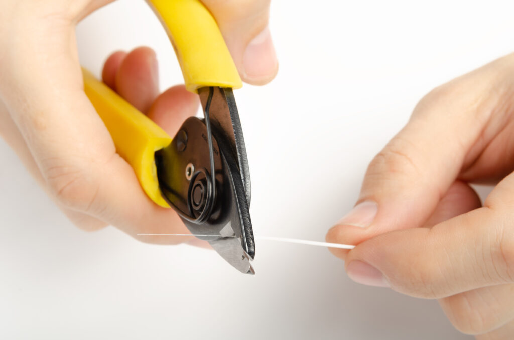 Two hands terminating a clear fiber with a pair of yellow clippers.